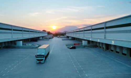 Imagem da área de docas de um galpão da GLP Brasil com carros e caminhões estacionados